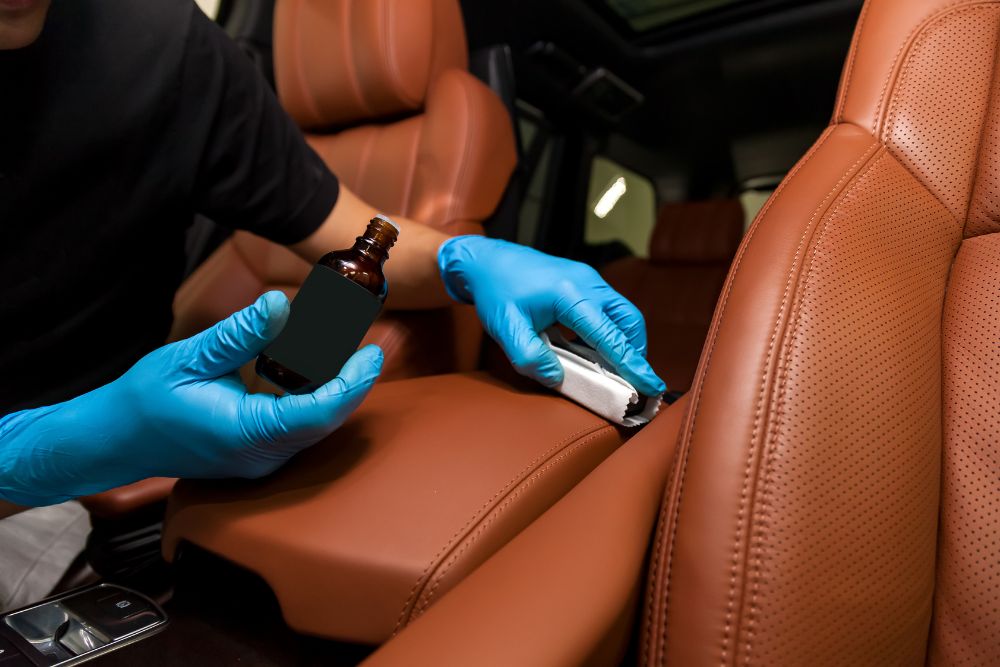 A man wearing blue gloves cleans leather using a bottle, demonstrating proper maintenance techniques for leather care.