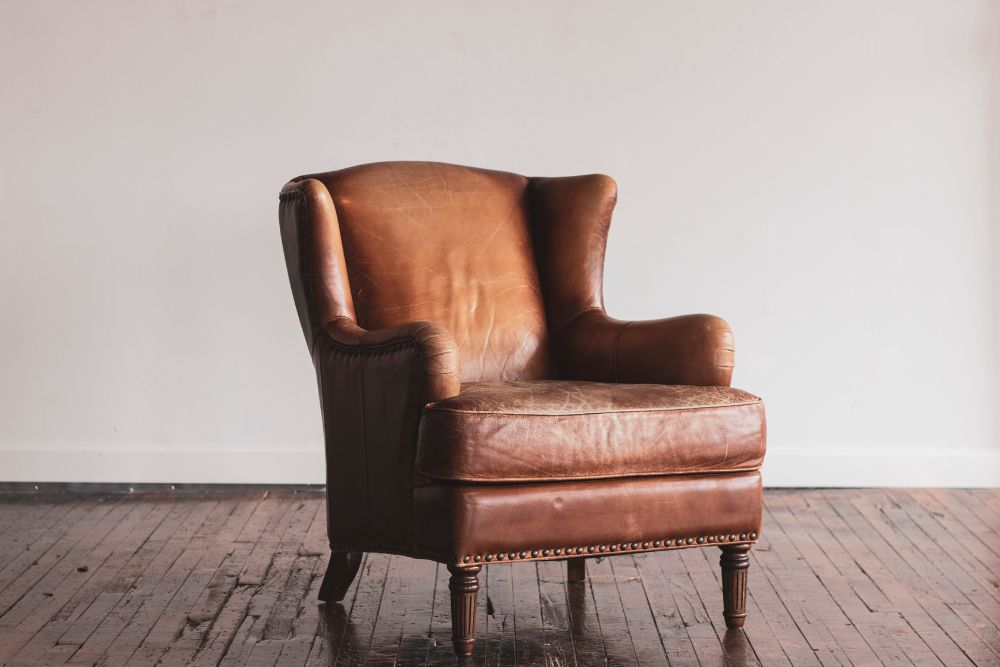 A solitary leather wingback chair in an empty room, showcasing its elegant design against a plain backdrop.