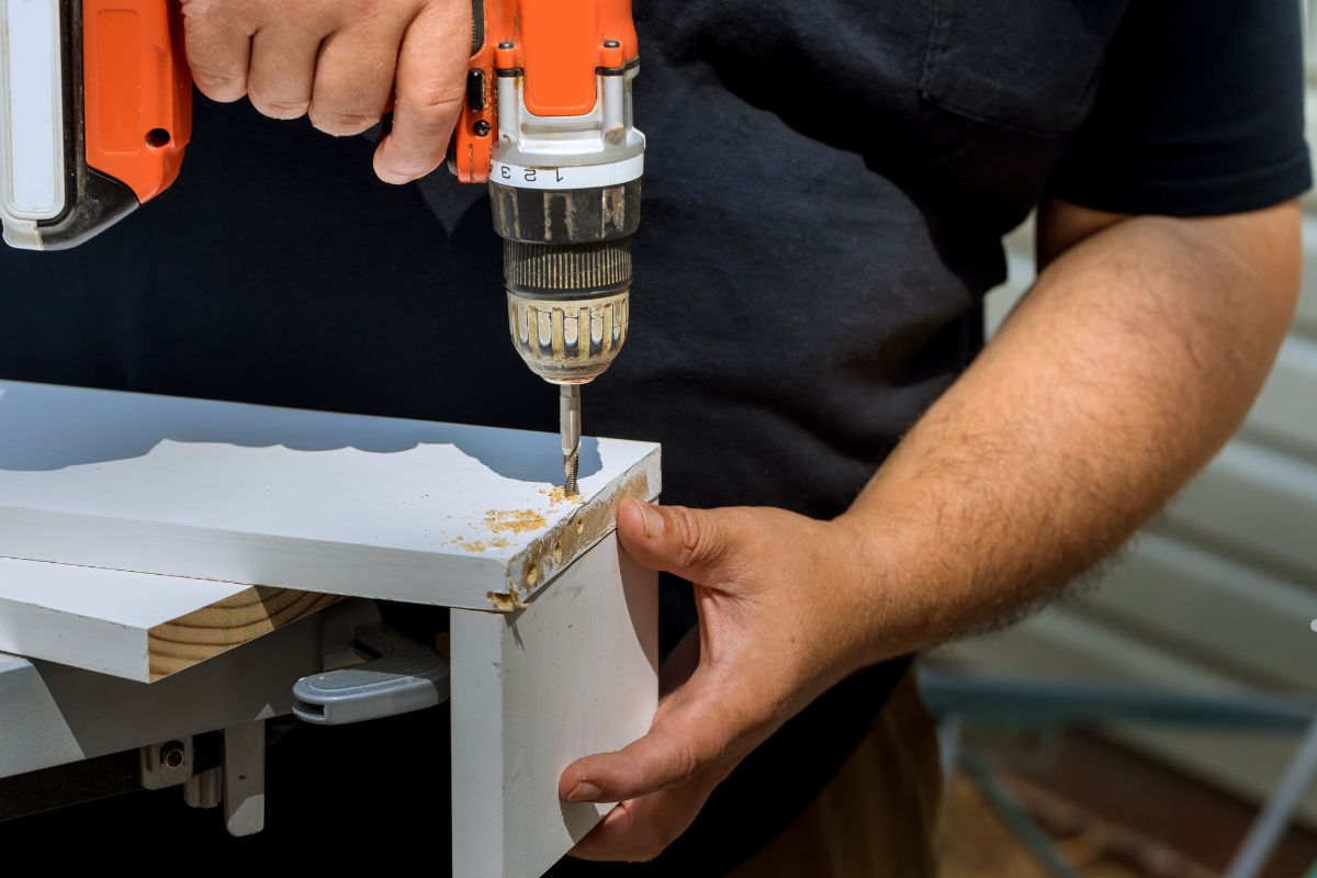 A man using a drill to secure a piece of wood to a table during a furniture repair service.
