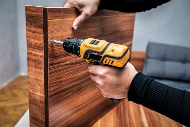 A person operates a drill, working on a wooden table as part of a furniture repair service.