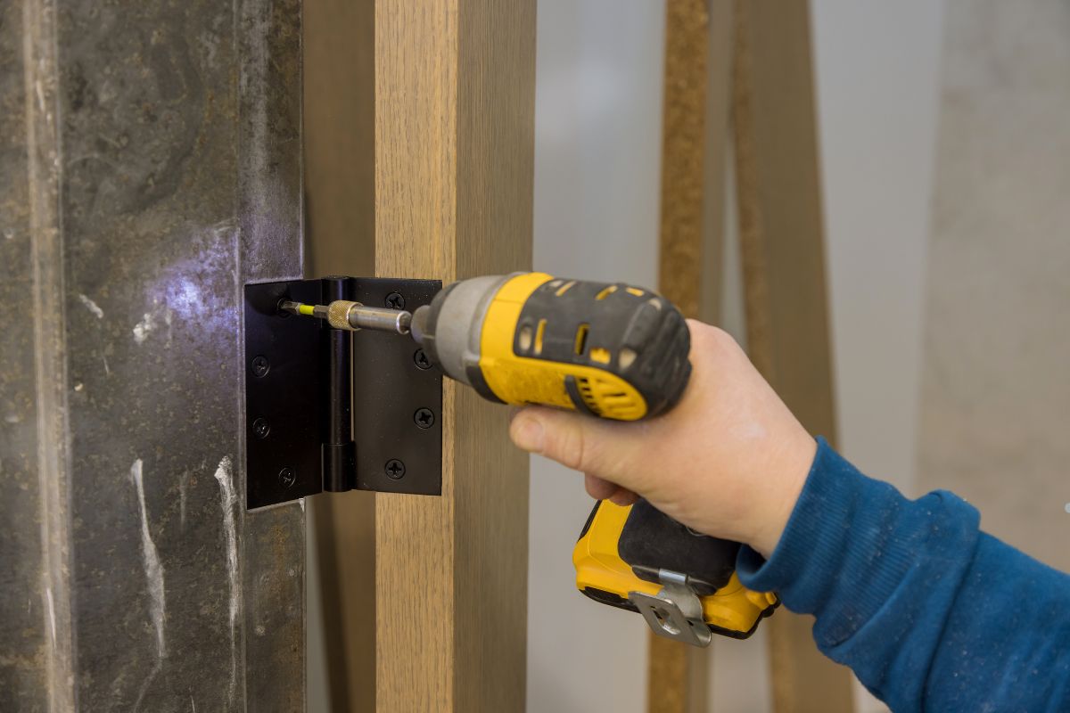 A person using a drill to secure a metal piece to a wall during a furniture repair service.